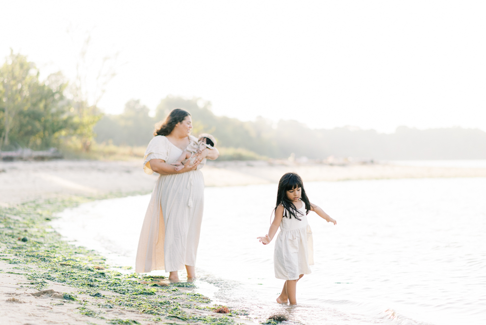 mom holding baby while daughter walks along the water at Virginia Beach