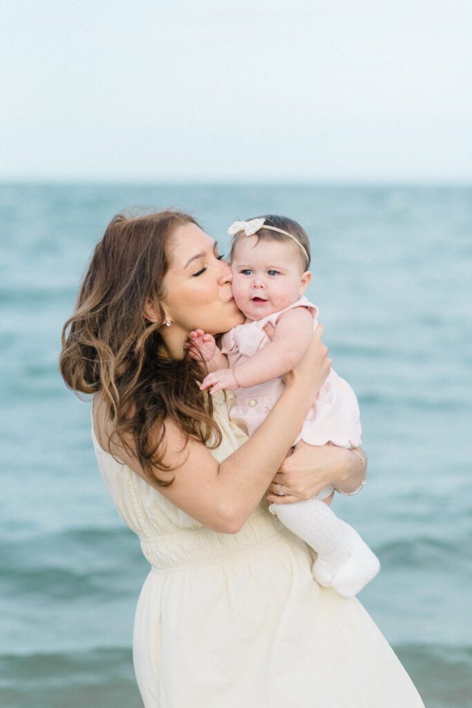 mom kissing baby girl wearing neutral dresses for Virginia Beach family photos