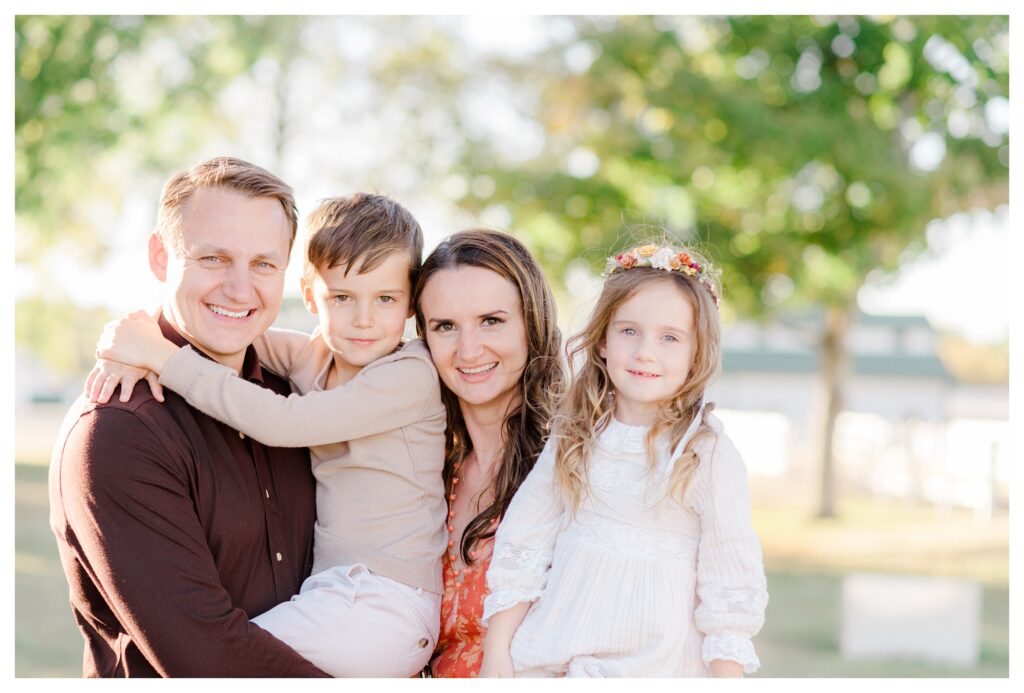 Family hugging and smiling at the camera during fall family photos in Williamsburg, Virginia