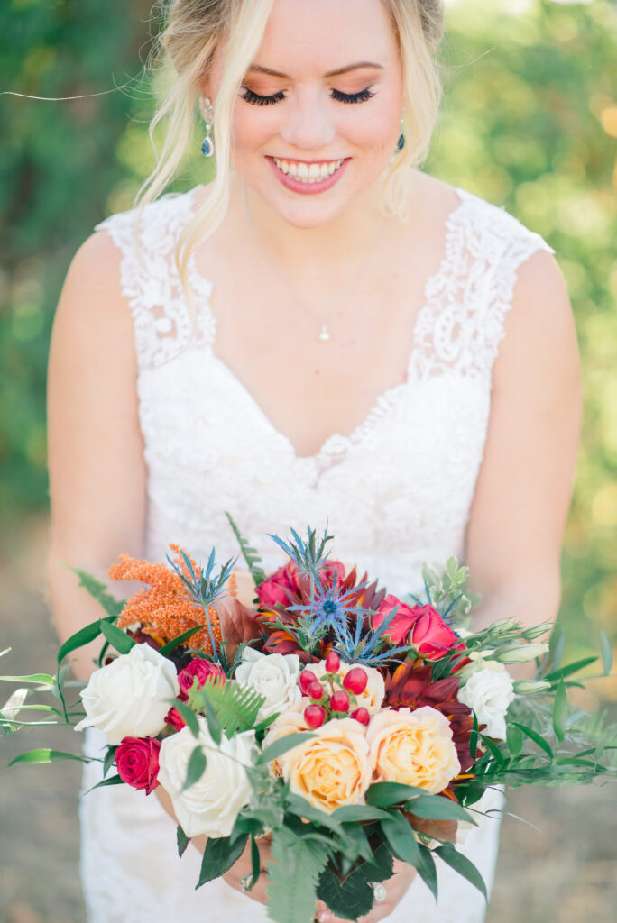 Bride smiles down at her colorful autumn wedding floral bouquet after eloping in Virginia Beach