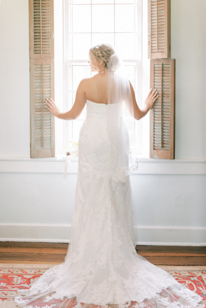 Bride looking out the window of her chateau bridal suite wearing a vintage lace wedding gown and veil