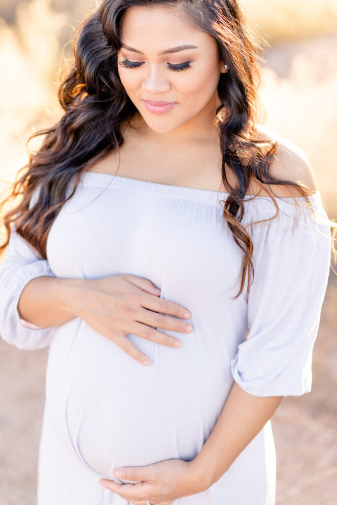 Sunset maternity photoshoot pose with mom holding hands on the belly