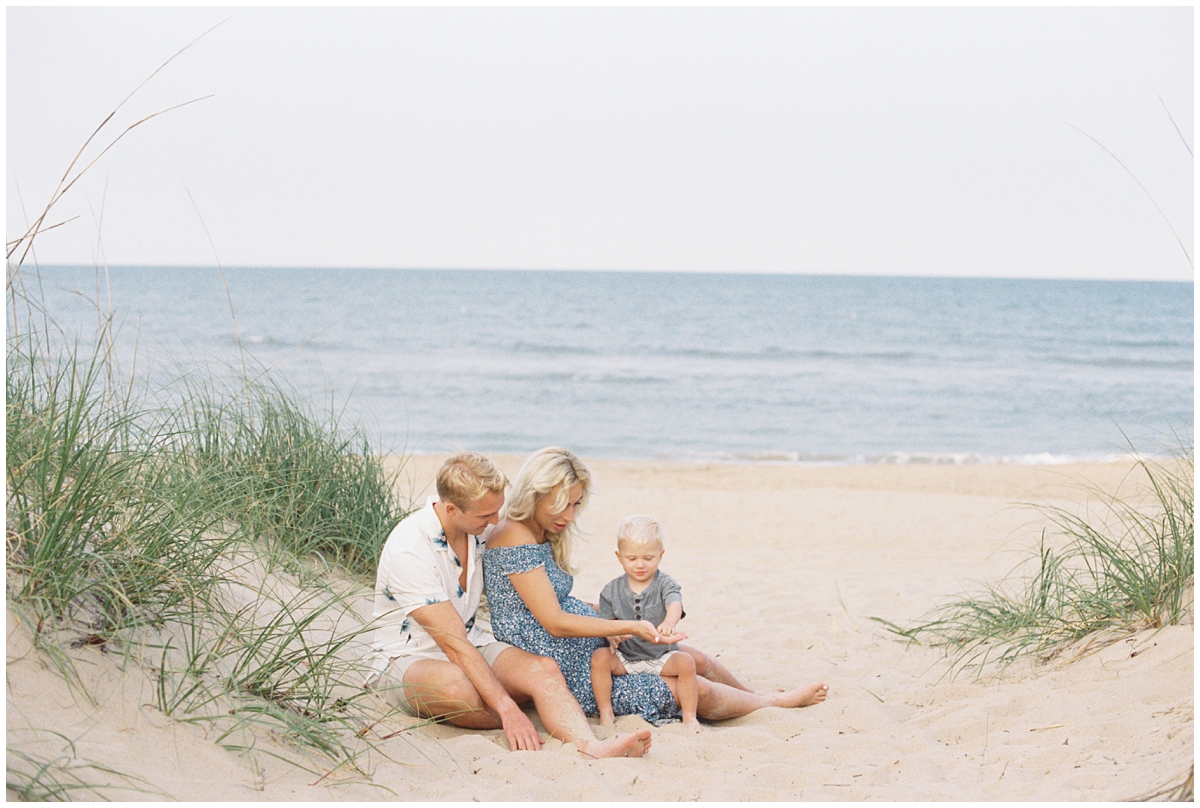 Family wearing blue and beige sitting in the sand at Croatan Beach, Virginia and playing with seashells