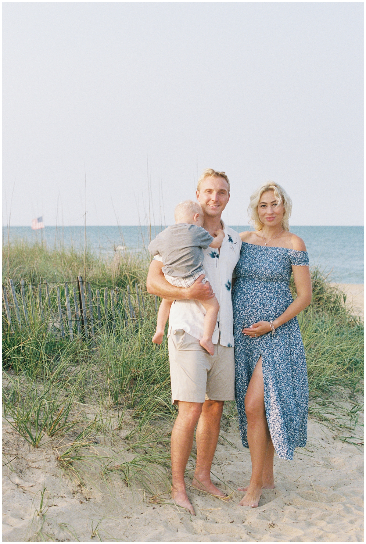 Sunset maternity photos in Virginia Beach with family wearing blue and white, standing in the sand dunes