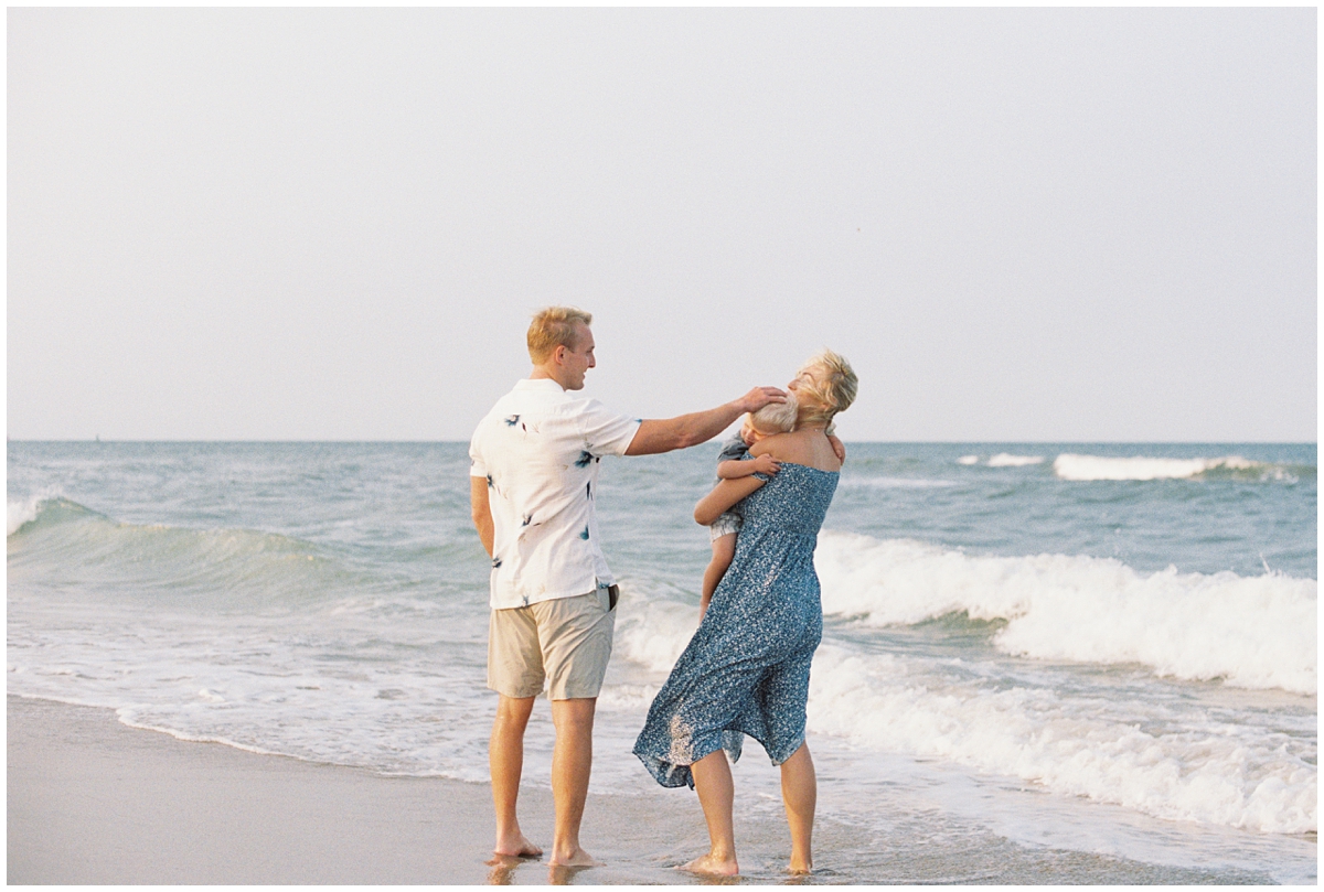 Dad reaching out to stroke son's hair as the sun sets over the dunes in Virginia Beach